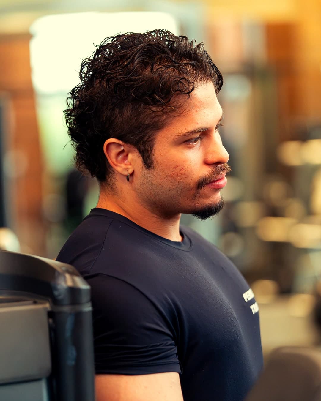 Theus Reis de perfil, na academia, com a camiseta de personal trainer